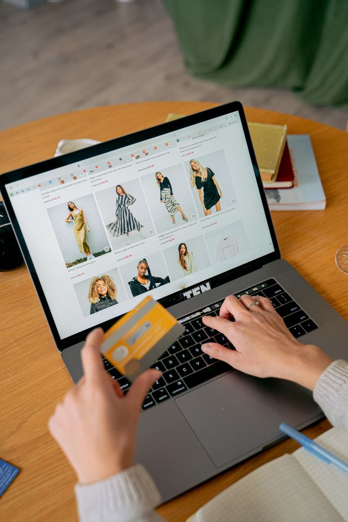 About A woman makes an online purchase using a credit card on her laptop, browsing an online fashion store.