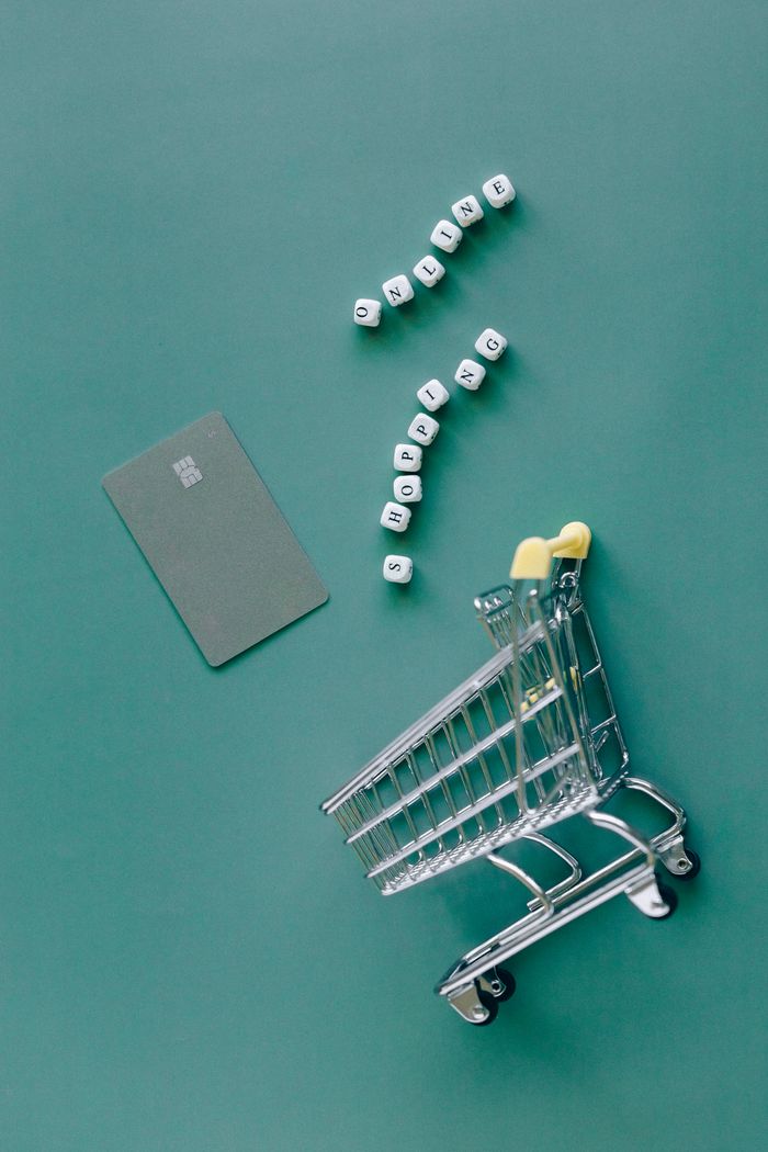 A conceptual image featuring a mini shopping cart, credit card, and letter blocks spelling 'online shopping' on a green background.