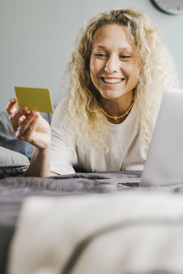 Blonde woman smiling while using a credit card and laptop indoors for online shopping.