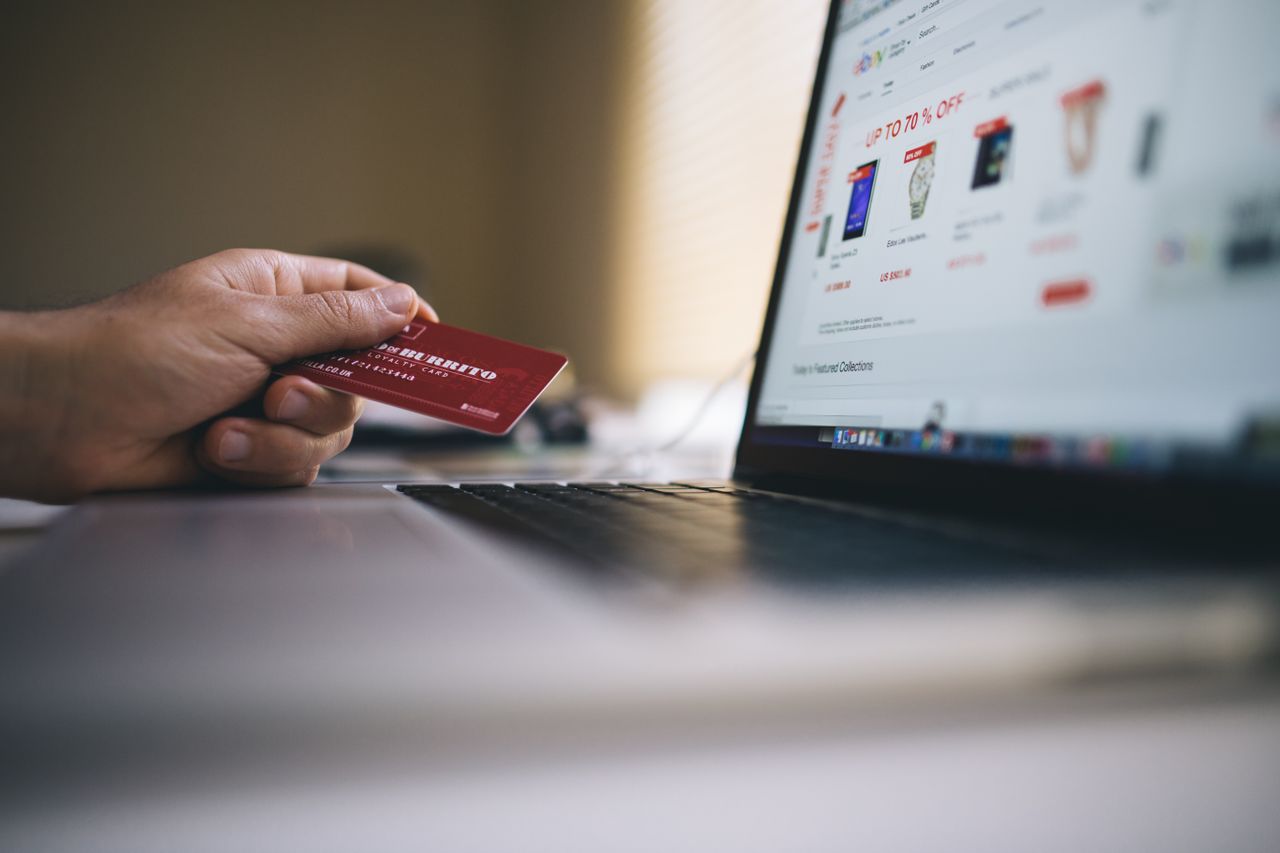 Services Person holding a credit card while shopping online on a laptop, indicating ecommerce transactions.